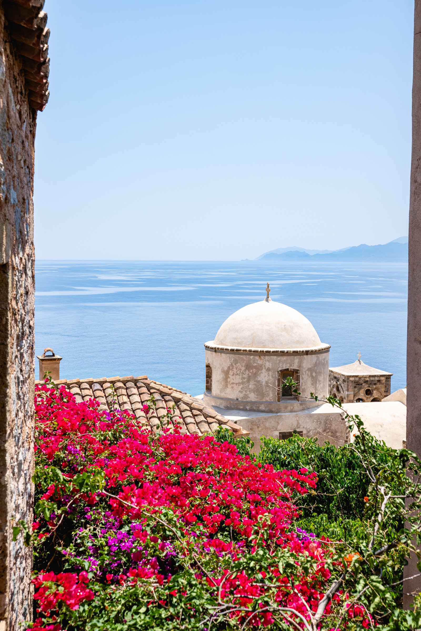 A Mediterranean church dome above the blue sea and flowering bougainvillea